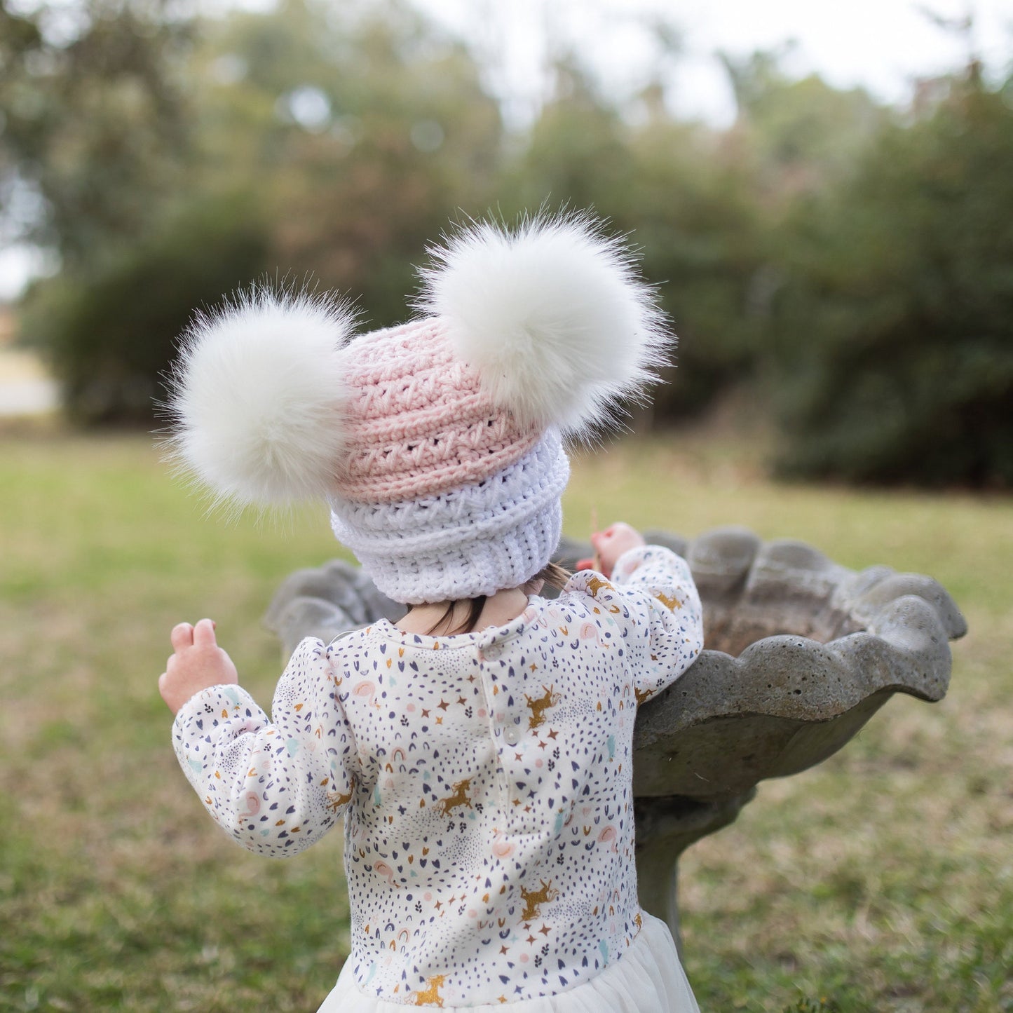 Back view of the white and pink beanie with two white faux fur pom poms