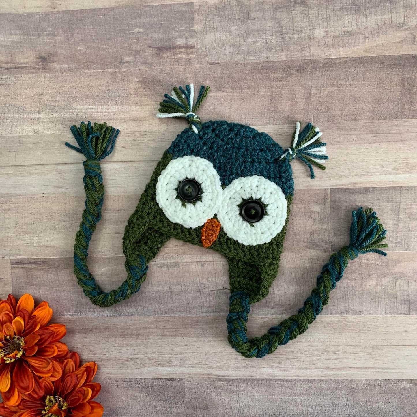 Teal and olive green owl beanie flat lay on a wooden background