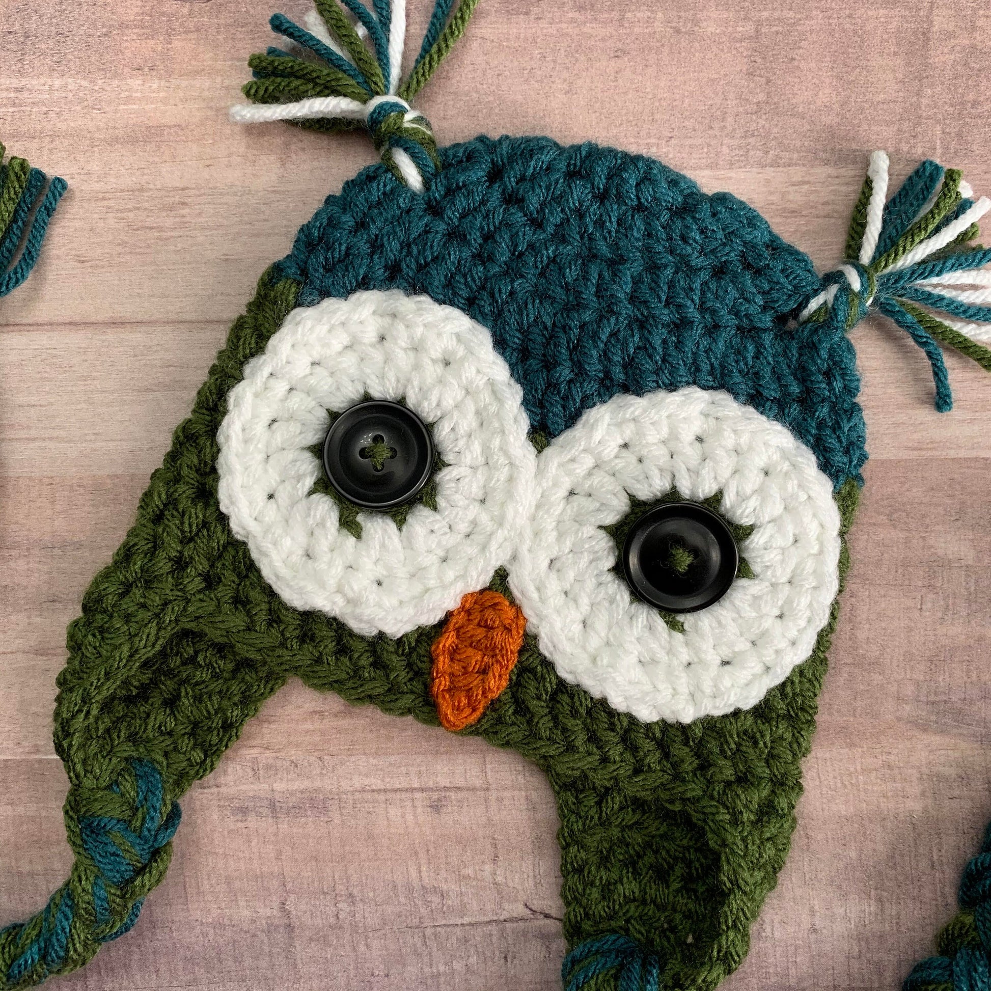 close up view of the owls face on a teal and olive green owl beanie