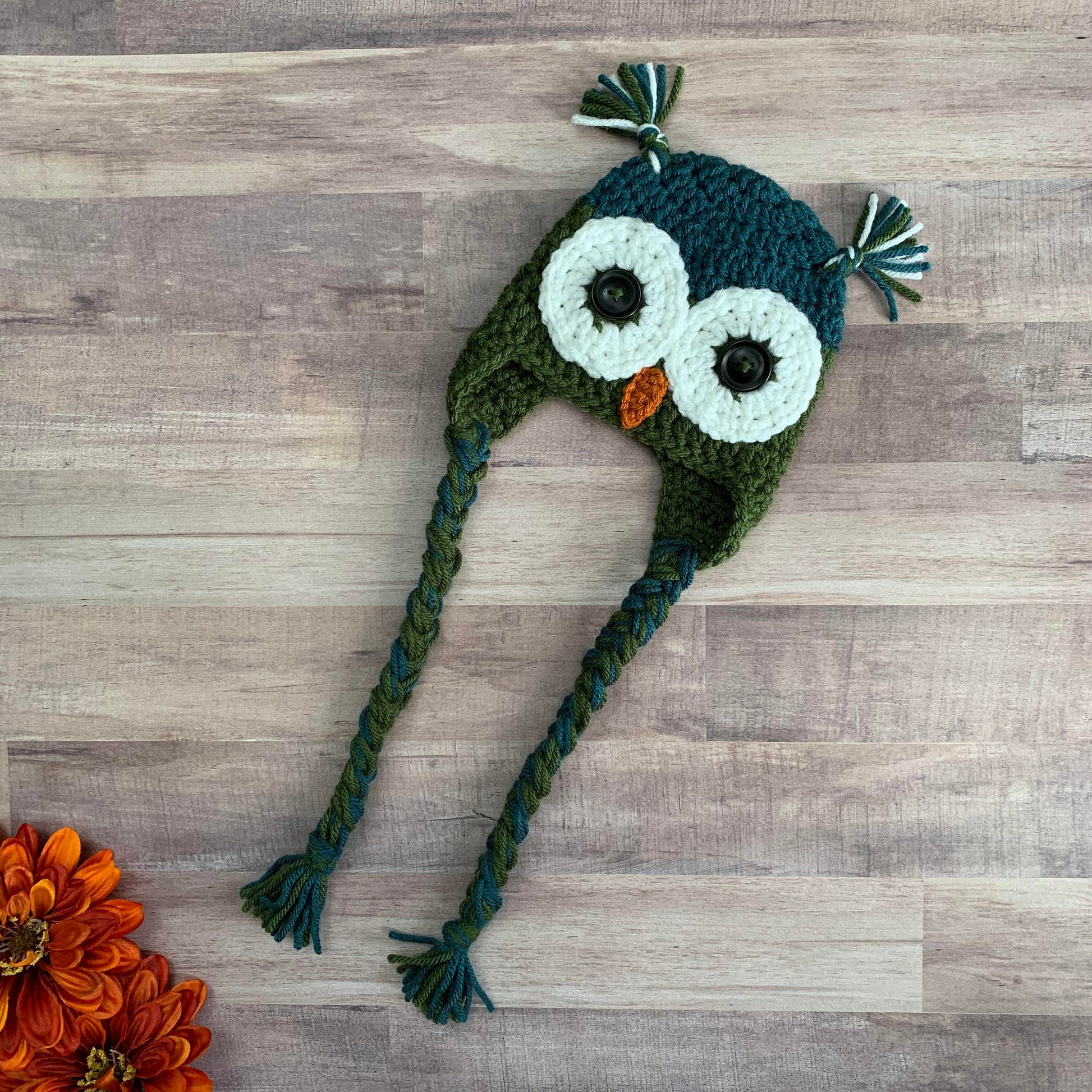 full length view of a teal and olive green owl beanie with braided ties and ear tassles