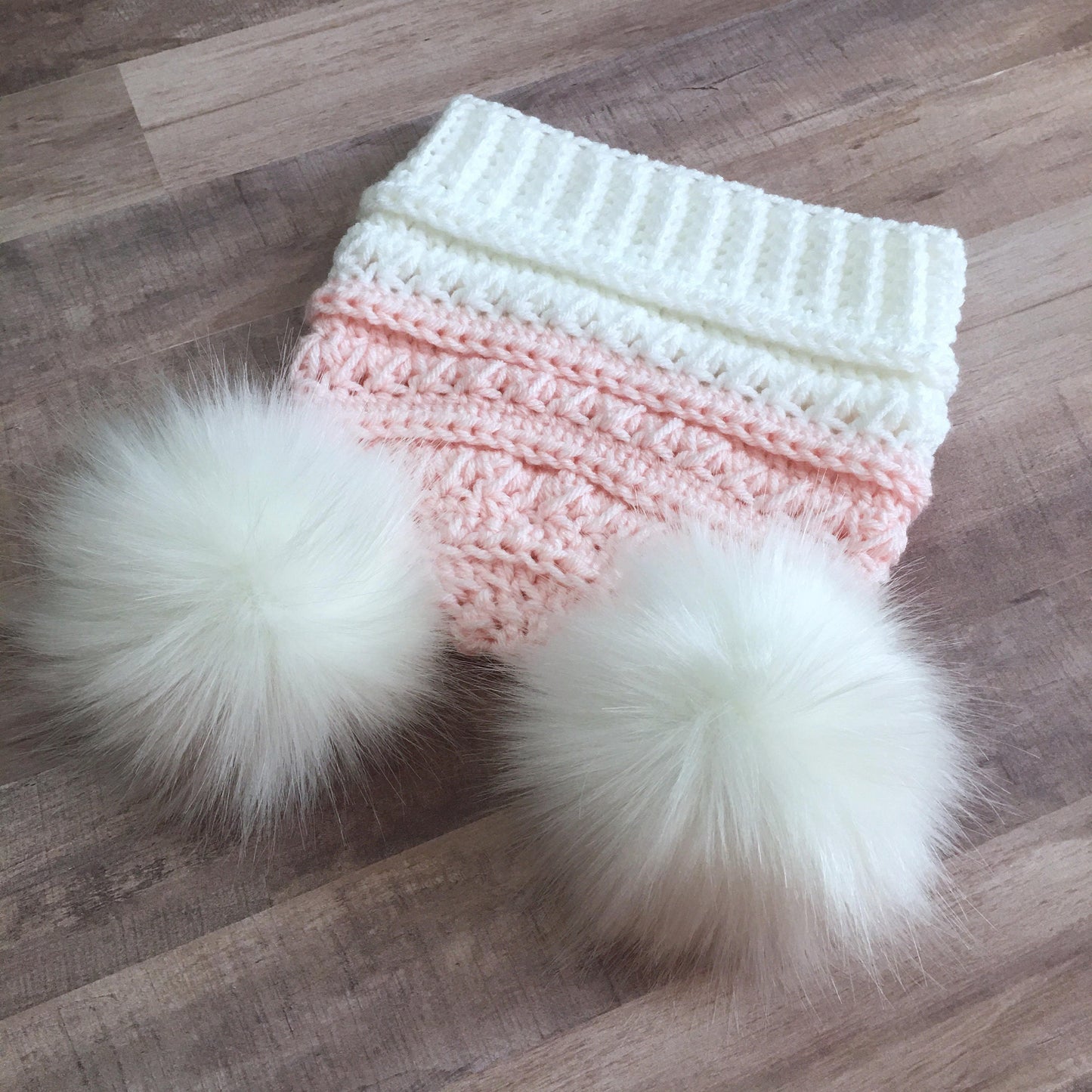 Top down view of this white and pink beanie with two white faux fur pom poms