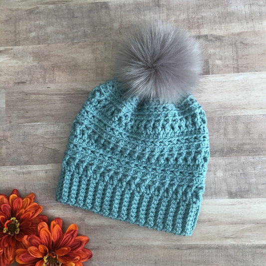 Blue textured beanie with a grey faux fur pom pom