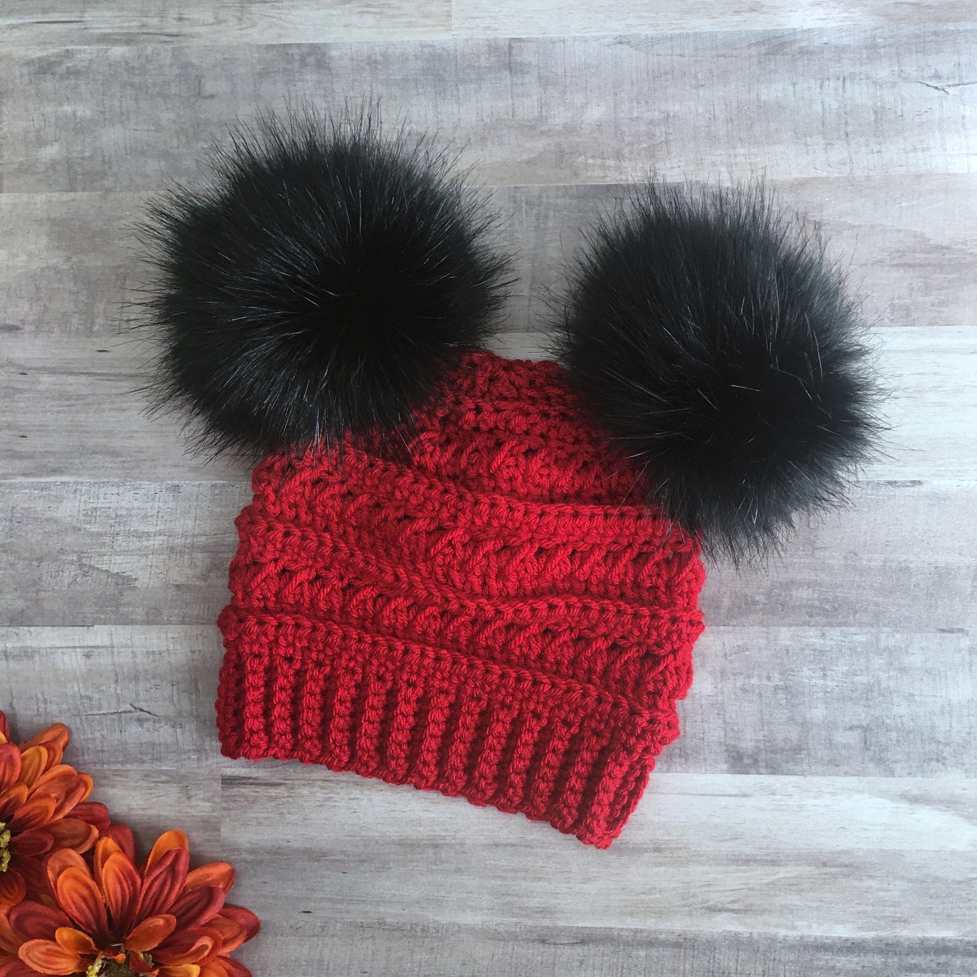 Red beanie with two black faux fur pom poms