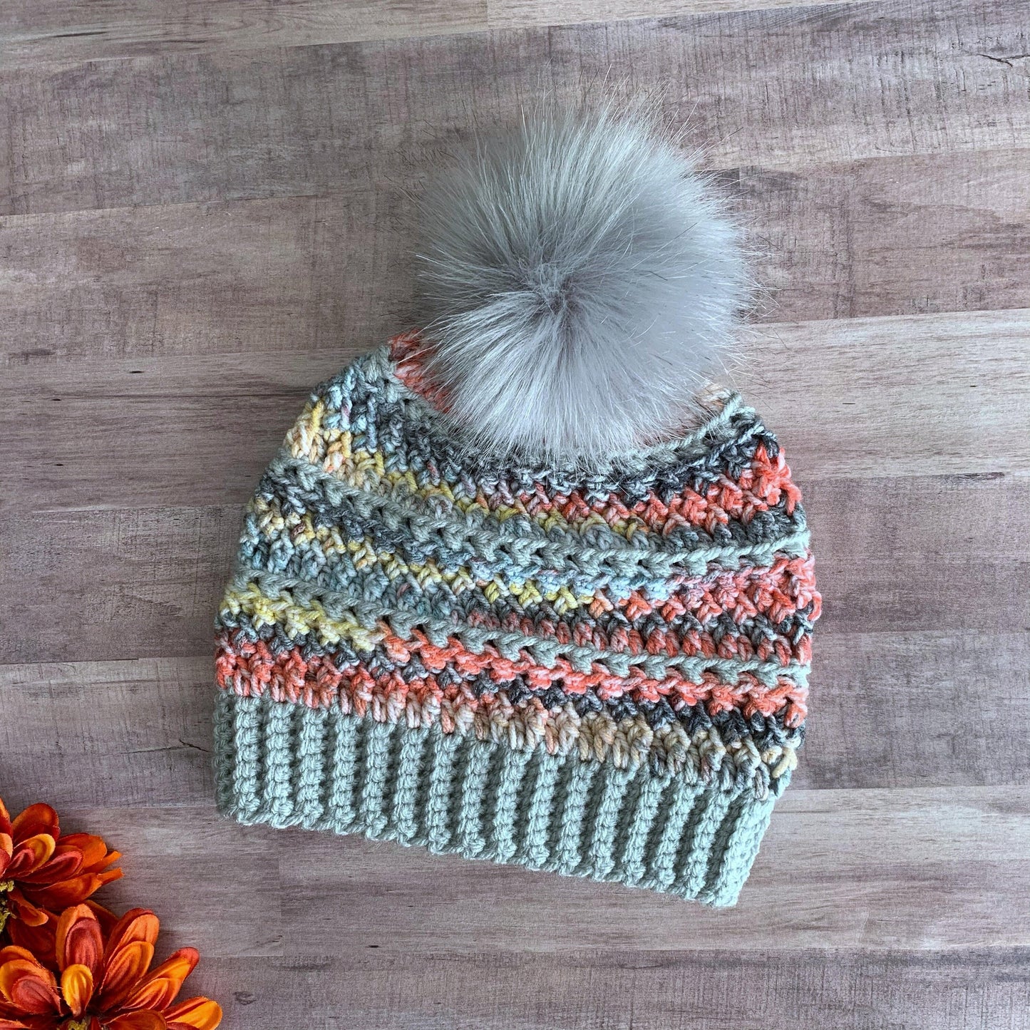 Grey rainbow beanie with a light grey faux fur pom pom