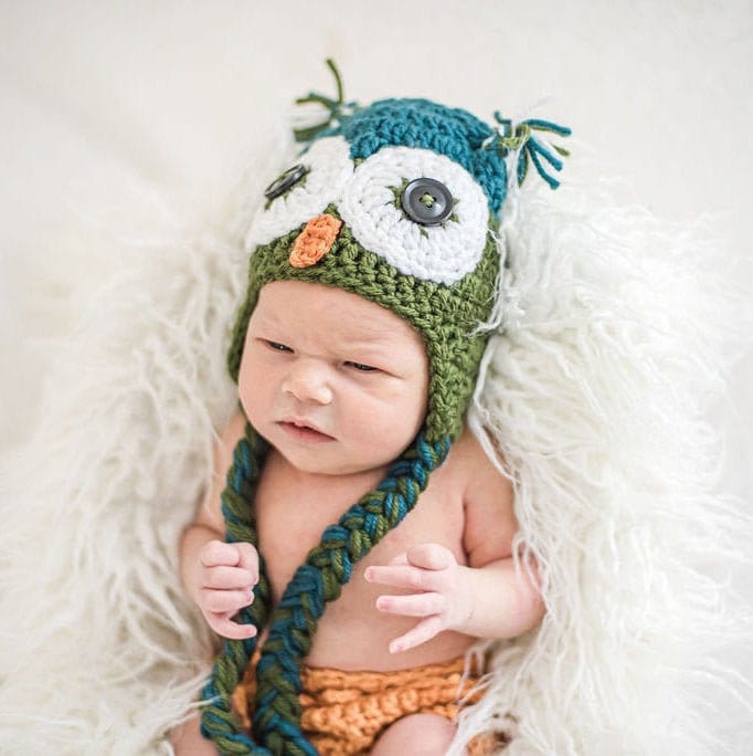 Newborn baby wearing a teal and olive green owl beanie