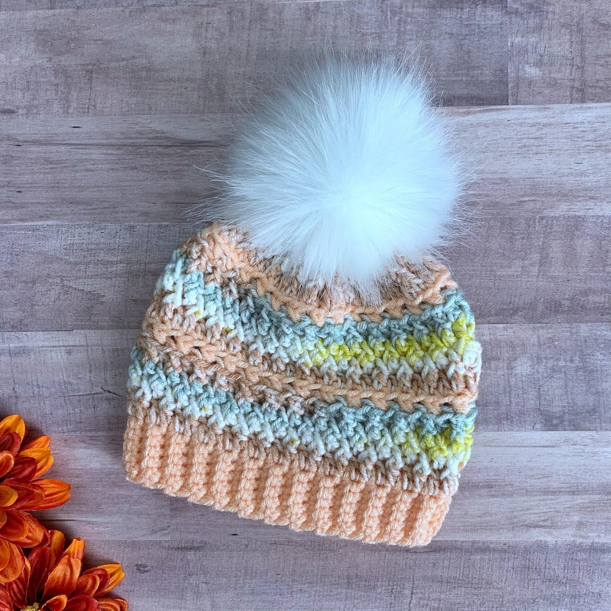 Colorful peach beanie with a white faux fur pom pom