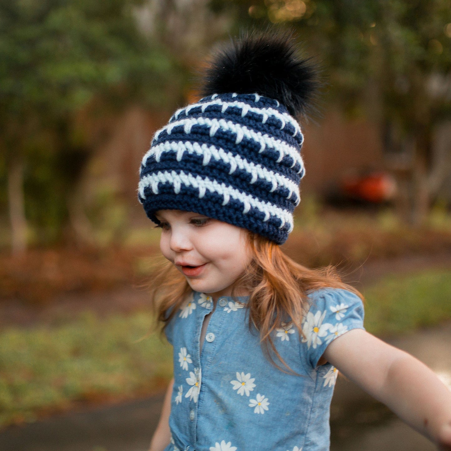 Side view of navy and arctic ice striped beanie with a black pom pom