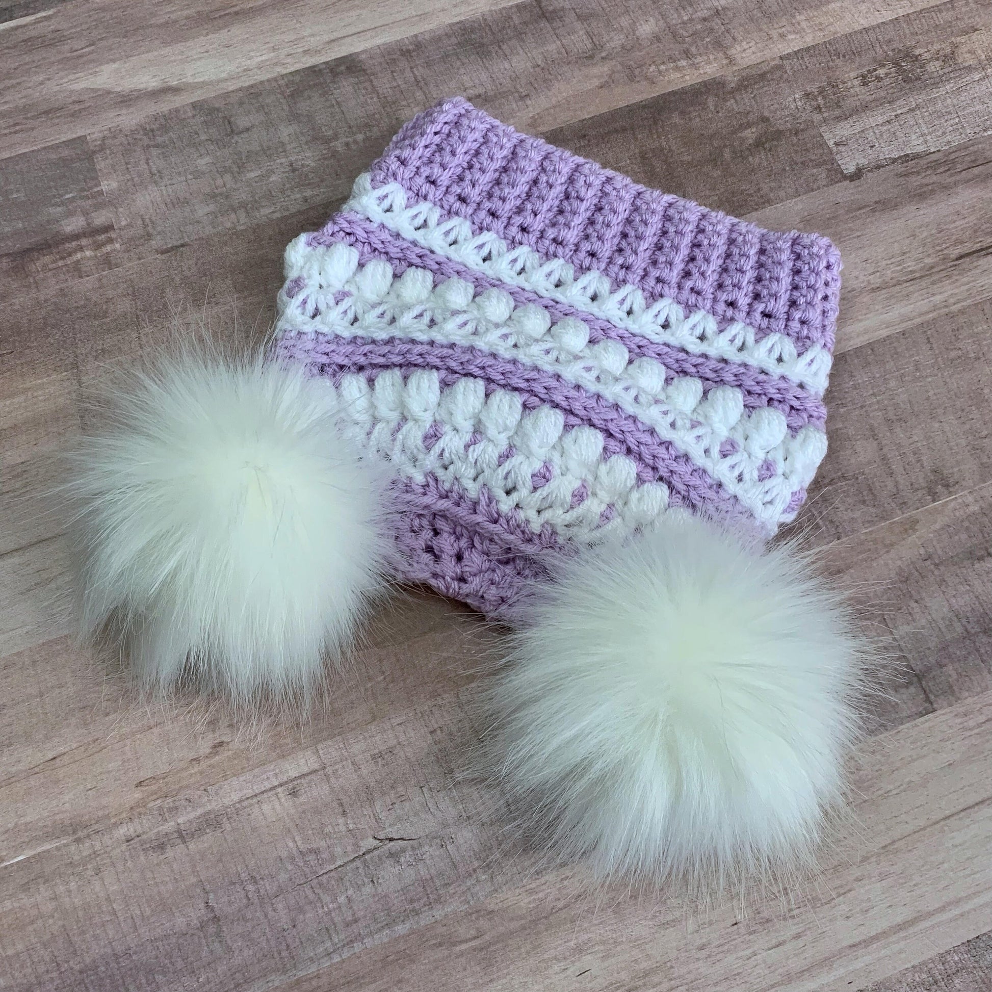 Top down view of this purple and white beanie with two white faux fur pom poms