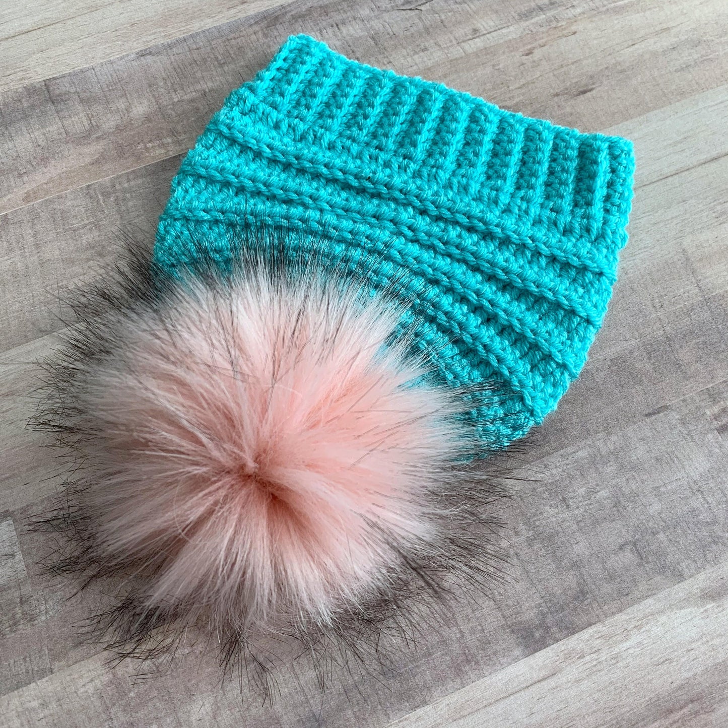 Head on view of the pink pom pom on this blue beanie